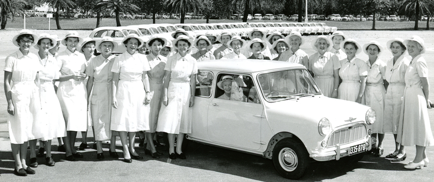 Many nurses wearing white surround a white car