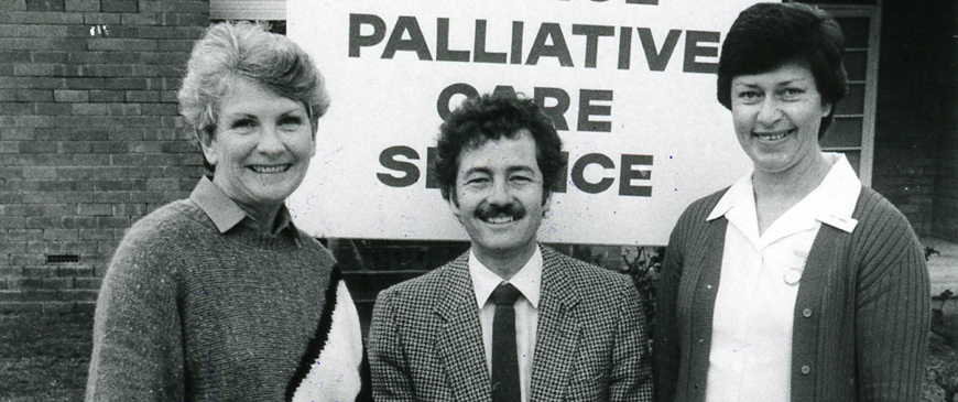 Three staff smile in front of palliative care sign